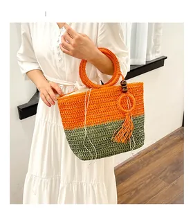Detail of hand-woven straw tote bag with orange and green patterns and tassel charm