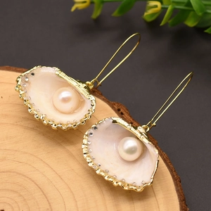 Elegant gold-plated shell pearl earrings on rustic wood background with leaf accents