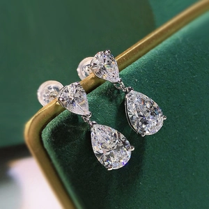 Macro shot of silver teardrop earrings with pear-cut stones on a green velvet box