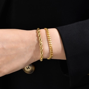 Close-up of gold rope and curb chain bracelets on a wrist with black suit jacket