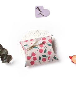 Detail of pink pillow gift box with cherry pattern and beige ribbon bow on lace paper