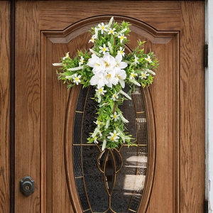 Easter cross wreath with white lilies and green leaves on a dark wooden front door