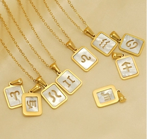 Macro detail of 18K gold zodiac necklaces with white shell inlay on beige fabric background