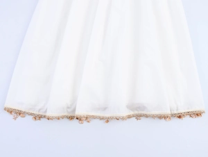 Detail of white beach dress hem featuring shell and starfish tassel fringe accents