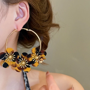 Detailed close-up of large golden hoop earrings with leopard print fabric flowers on model