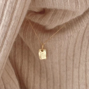 Close-up of golden rectangular 'be loved' pendant necklace on a knit sweater background
