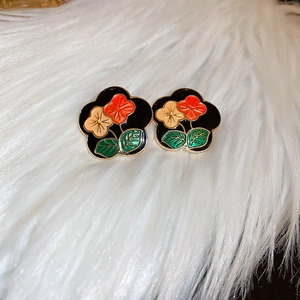 Detailed close-up of retro floral enamel earrings with gold plating on soft white plush