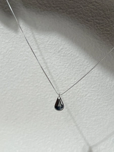 Macro detail of a minimalist silver teardrop pendant necklace with a polished mirror finish