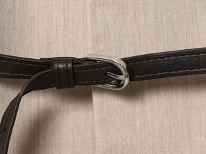 Close-up of a dark brown leather belt with a silver pin buckle on beige blazer fabric