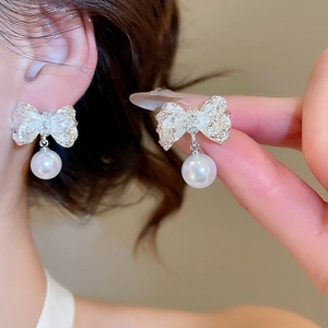 Gros plan de boucles d'oreilles nœud argenté avec perles blanches portées par un mannequin
