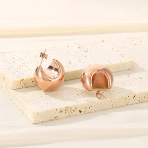 Detail of rose gold thick hollow half-hoop earrings on a natural travertine stone base