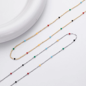 Detail of gold and silver dainty chains with colorful beads on a white ceramic plate