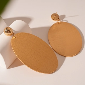 Detail of gold oval geometric earrings showing brushed metal texture and round studs