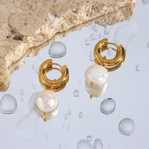 Détail macro de boucles d'oreilles perles baroques dorées sur surface d'eau réfléchissante