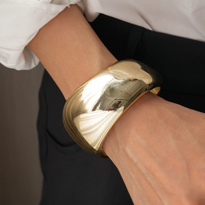 Close-up of a wide chunky gold metal cuff bracelet worn with a professional white shirt