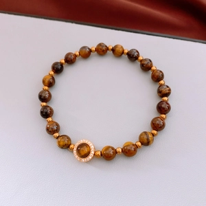 Détail macro du bracelet en perles d'œil de tigre avec pendentif gourde dorée et zircons