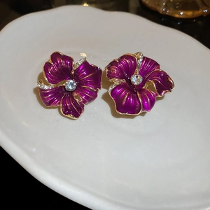 Gros plan de boucles d'oreilles fleurs mauves avec bords dorés et cristaux sur un plateau