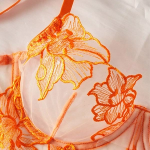 Detail of vibrant orange embroidered lace on a sheer mesh bra cup with floral patterns