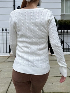Back view of a white cable knit long sleeve sweater for women in an outdoor setting