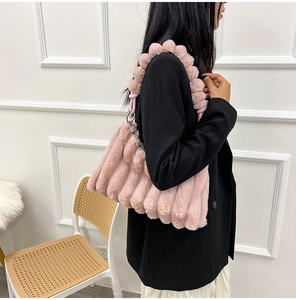 Close-up of pink plush shoulder bag with vertical pleats and soft pompom decoration