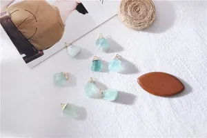 Macro shot of 8 natural green raw fluorite crystal pendants with golden bails on white linen