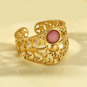 Macro detail of gold open ring featuring filigree patterns and a round pink stone