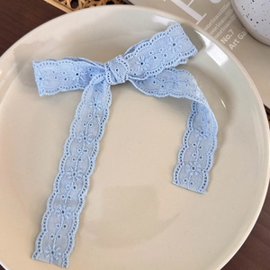 Detail of light blue lace bow hair clip with embroidery on a cream ceramic plate