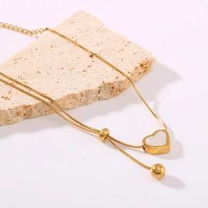 Gold heart pendant necklace with white seashell inlay on a minimalist stone base