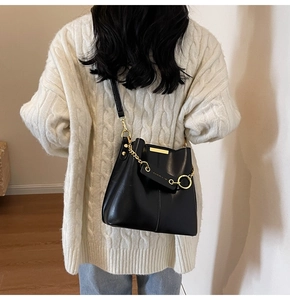 Model wearing black leather bucket bag with gold chain strap back view on white sweater