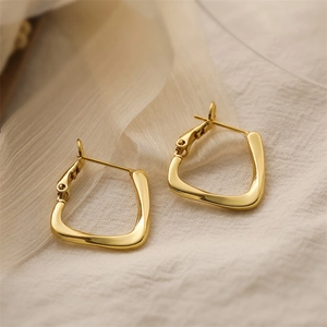 Detail shot of golden C-shaped geometric earrings on elegant beige wrinkled fabric