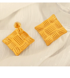 Macro detail of gold square stud earrings with unique woven texture on soft white fabric