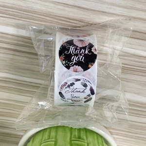 Detail view of round floral Thank You stickers roll in transparent plastic packaging