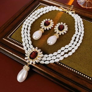 Detail of floral crystal necklace and drop pearl earrings on green velvet background