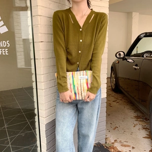 Detail of colorful striped woven clutch bag paired with green knit cardigan outdoors