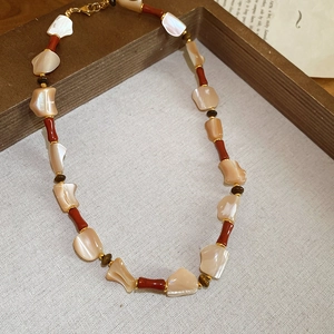 Close-up of beaded necklace with irregular mother-of-pearl and red resin stones