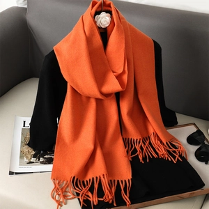Detail of soft orange pashmina scarf with fringe edge on a black coat with magazine