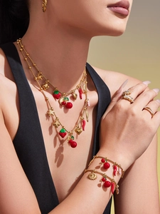Gros plan d'un mannequin portant des colliers et bracelets en or 18K avec breloques fruits