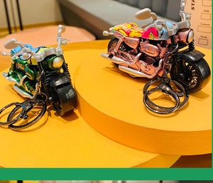 Close-up of colorful cartoon motorcycle keychains in green and pink on a yellow display