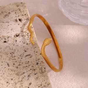 Detailed macro of golden snake open bracelet with engraved scales on travertine stone