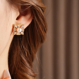 Close-up of a gold square stud earring with a white pearl and sparkling zircons on ear