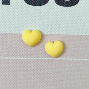 Gros plan de deux breloques cœurs jaunes mats sur fond texturé rose pour DIY bijoux