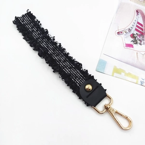 Black woven bag strap with silver silk thread, leather trim, and gold tassel accessory