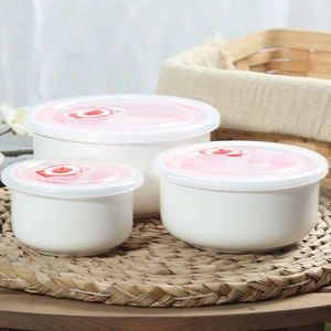 Three round white ceramic storage bowls with transparent lids on a straw mat
