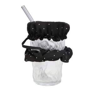 Detail of black fabric drink cover with silver dots and elastic band on glass with straw