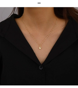 Close-up of gold heart lock pendant and delicate figaro chain worn on a model