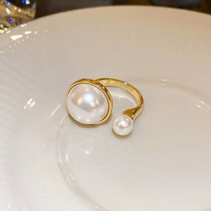 Close-up of gold-plated open ring with two white pearls on a white ceramic plate