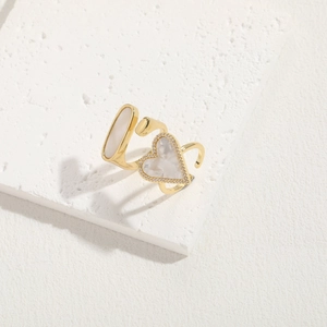 Golden open ring with shell heart and oval inlay on a white stone pedestal