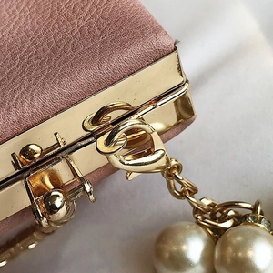Detailed close-up of golden hardware clasp and pearl charm on a pink leather handbag
