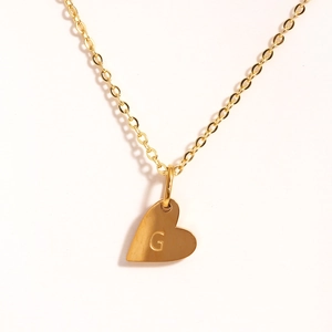 Détail du pendentif cœur doré avec la lettre G gravée sur chaîne en acier inoxydable