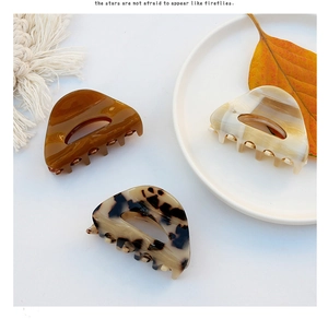 Three acetate claw clips in amber, cream marble, and tortoiseshell on a white plate